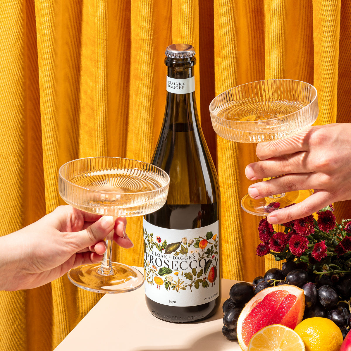 Cloak & Dagger Prosecco bottle with two coupe glasses, fresh fruit and flowers, perfect for stylish celebrations and gifting from the Wine and Extra WOW collections