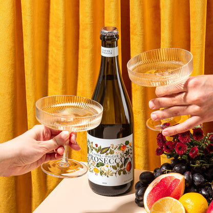 Cloak & Dagger Prosecco bottle with two coupe glasses, fresh fruit and flowers, perfect for stylish celebrations and gifting from the Wine and Extra WOW collections