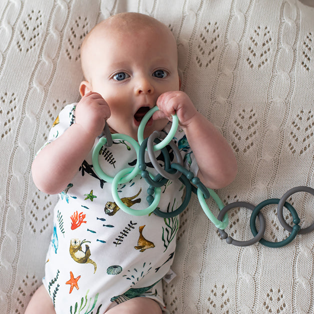 Mum & Baby Gift Hamper featuring a happy baby holding a soft teething toy on a knitted blanket for a thoughtful new baby gift