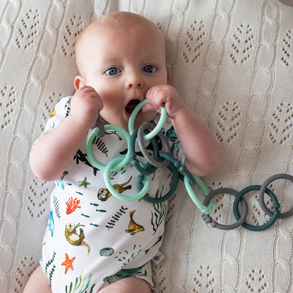 Mum & Baby Gift Hamper featuring a happy baby holding a soft teething toy on a knitted blanket for a thoughtful new baby gift