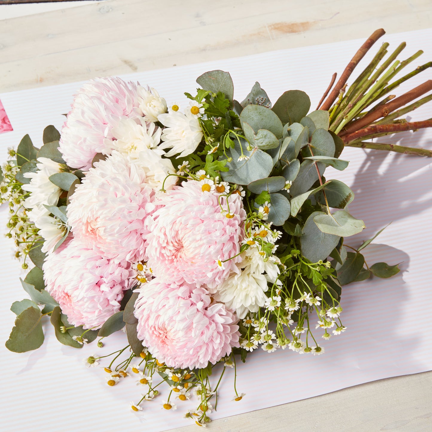 Soft pink chrysanthemums and white daisies with eucalyptus foliage arranged as a fresh bouquet on pale paper for special occasion flowers and gifting
