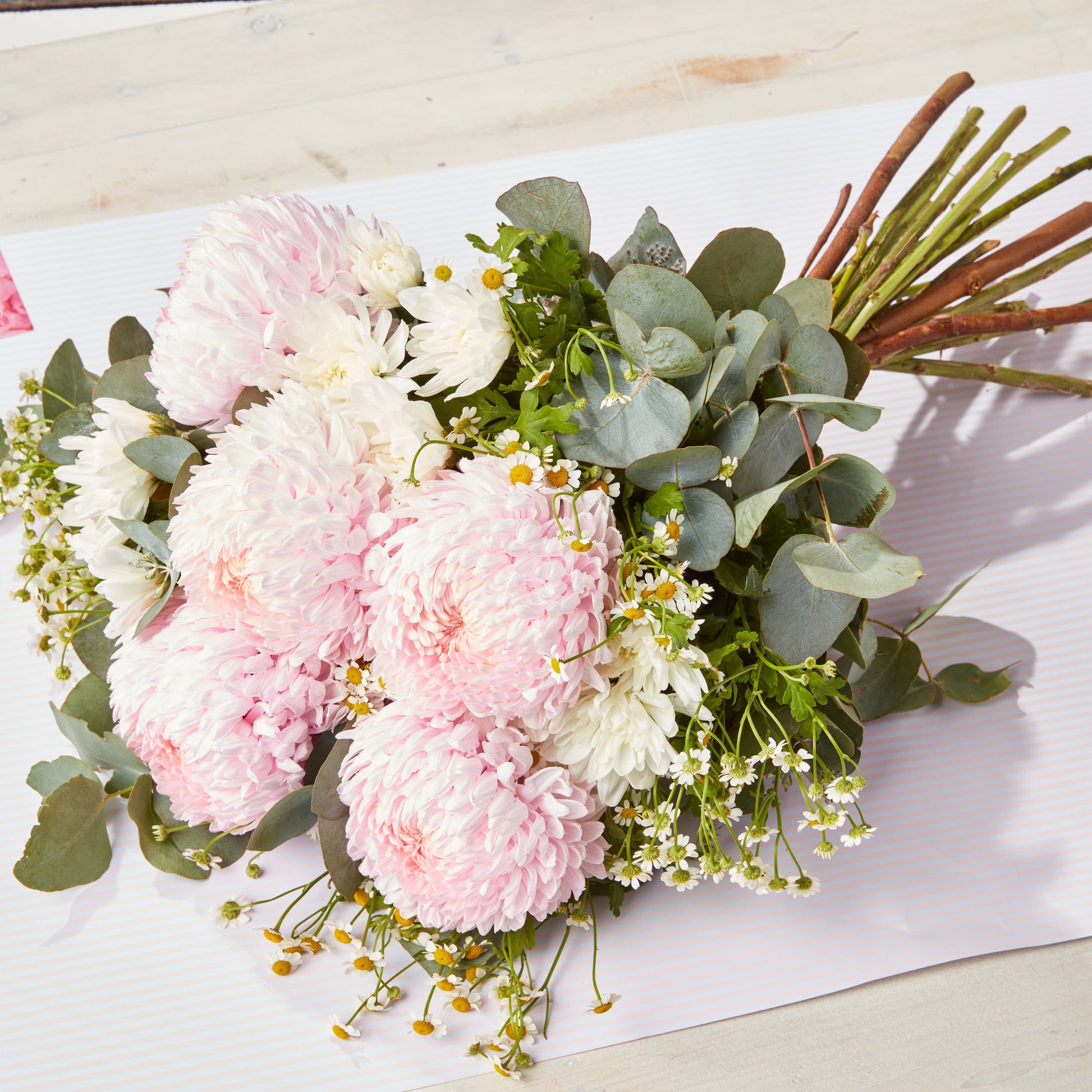 Soft pink chrysanthemums and white daisies with eucalyptus foliage arranged as a fresh bouquet on pale paper for special occasion flowers and gifting