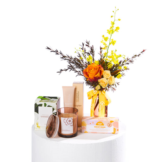 Sunshine Bliss Hamper with orange and yellow flowers in a vase alongside candles and gourmet treats for bright gifting and same day delivery